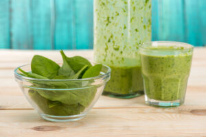 Ein Glas grüner Smoothie, danaben ein Glasshälchen mit frischem Spinat