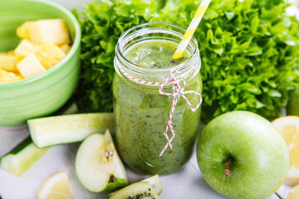 Ein Glas grüner Smoothie neben Äpfeln und Salat.