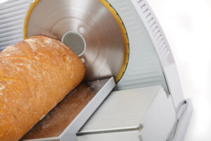Eine Brotschneidemaschine, auf der ein Brot geschnitten wird.