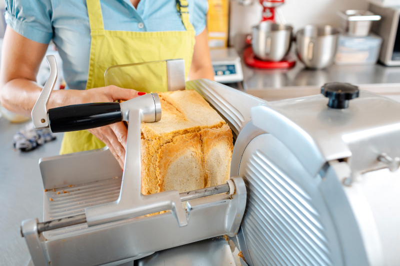 Eine Frau in gelber Schürze schneidet Brot in einer Brotschneidemaschine.