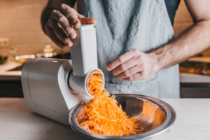 Ein Mann raspelt Karotten in einer Küchenmaschine